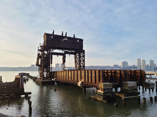 A rusting transfer bridge sits in the water, surrounded by pilings from long-gone piers.