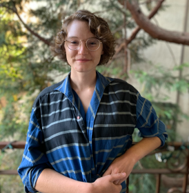Kat stands on a balcony with trees in the background