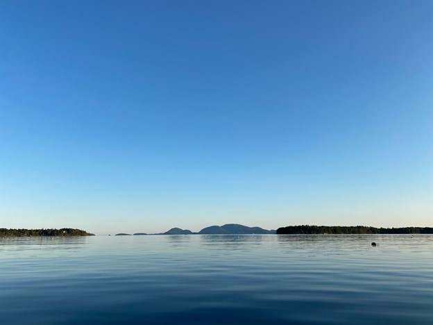 Calm blue water and a blue sky frame the silhouette of mountains and islands in the distance.