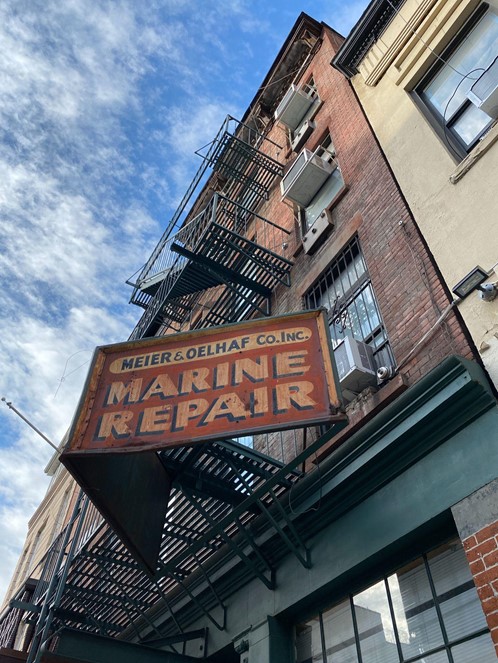 Alt text: A rusted red sign on a brick building reads "Meier & Oelhaf Co. Inc., Marine Repair."