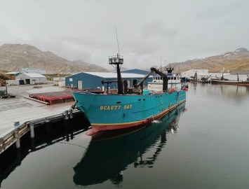 a bright blue longline catcher processor tied up to a dock in Dutch Harbor, Alaska.