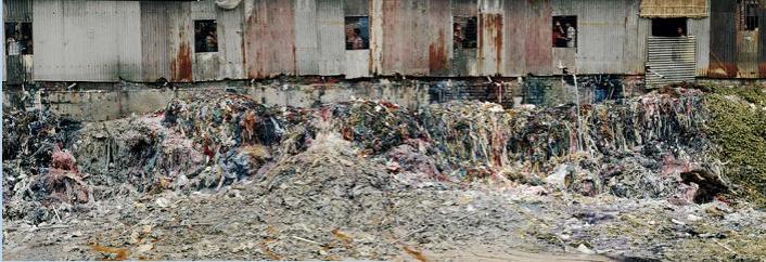 A large pile of textile waste in front of a factory.