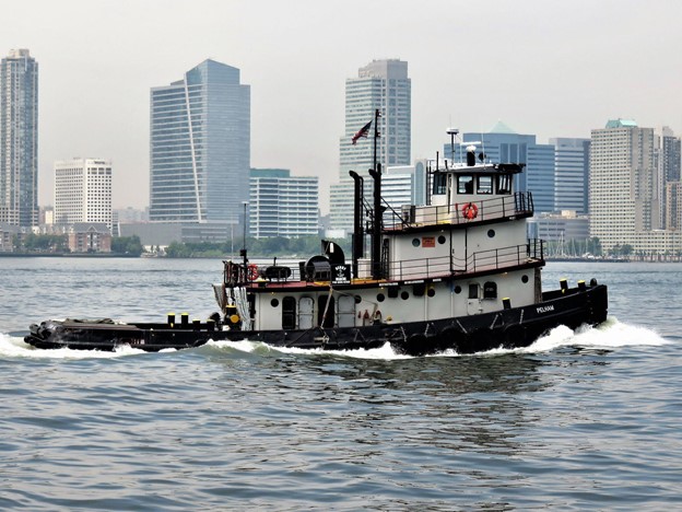 A tugboat under way, with New Jersey skyscrapers in the background.
