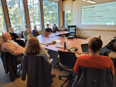 Students and audience sit around a u-shaped table to discuss their capstone project.