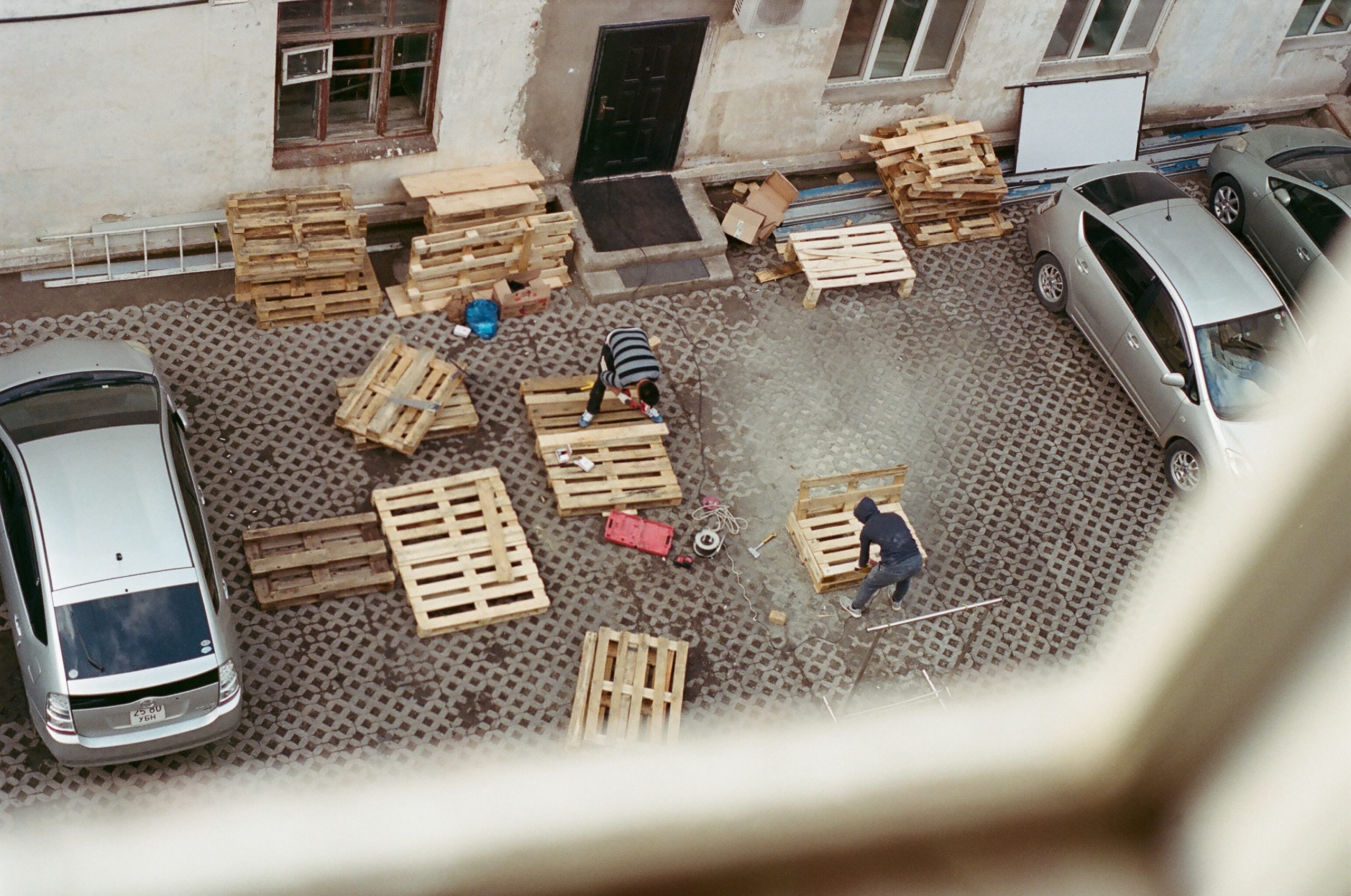 Looking from above, a photo shows a courtyard stacked with pallets and a few figures working to cut them apart.