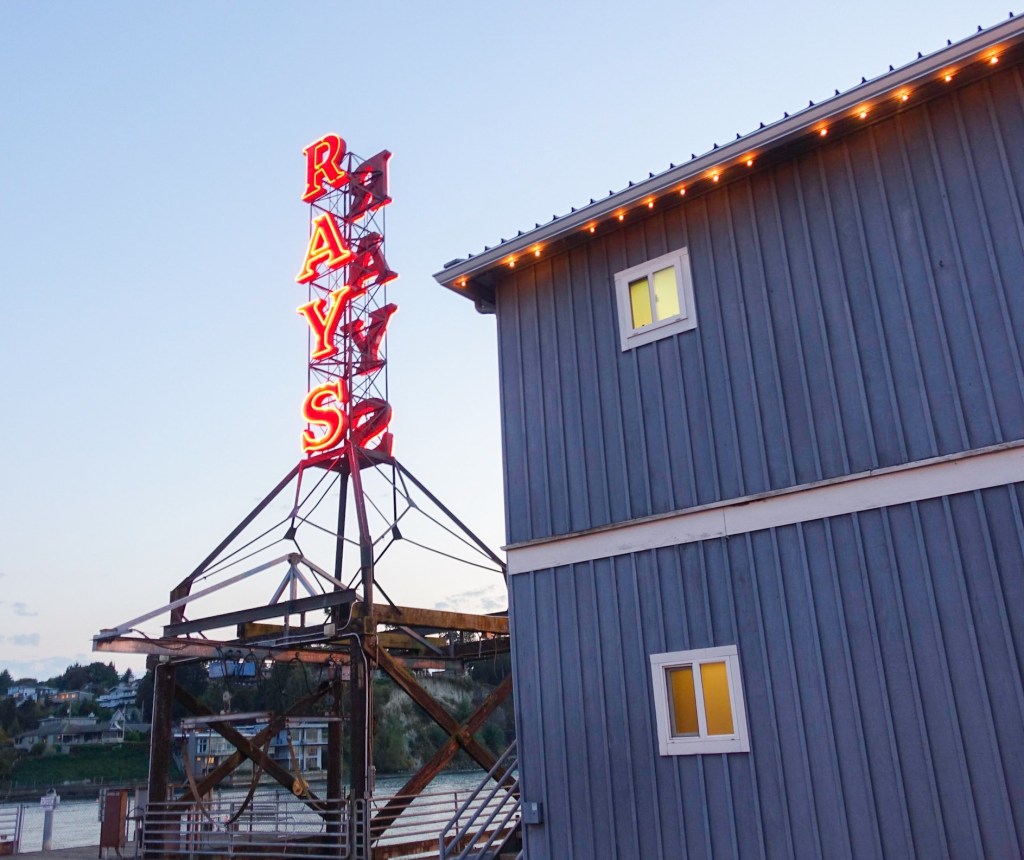 A neon red "RAY'S" sign sticks up next to a blue-grey building.