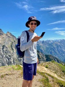Jack smiling atop a mountain on a beautiful sunny day in the North Cascades - flip phone in hand.