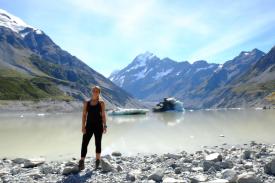 Olivia stands on the edge of a lake with mountains in the background