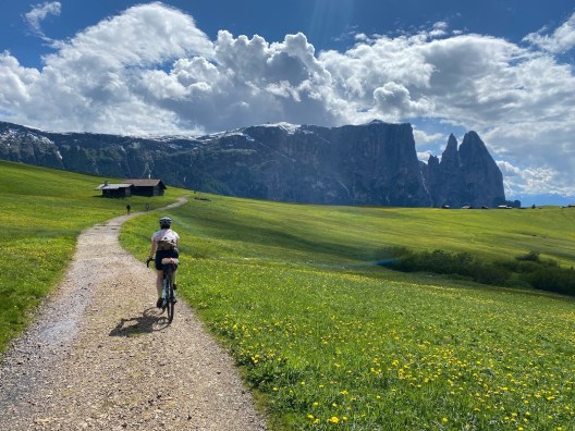A biker heads down a dirt path through an extraordinarily green field towards a striking cliff line in the distance.
