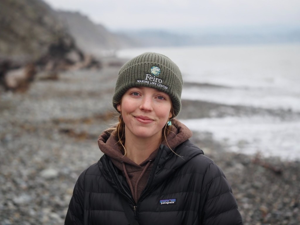 Alt text: A headshot of Emily Bews in front of a rocky shoreline