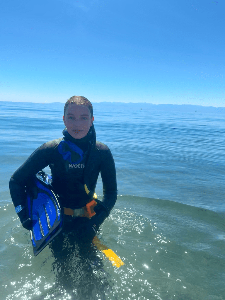 Alt text: A photo of Emily Bews in snorkel gear, standing waist-deep in water and holding a pair of fins.
