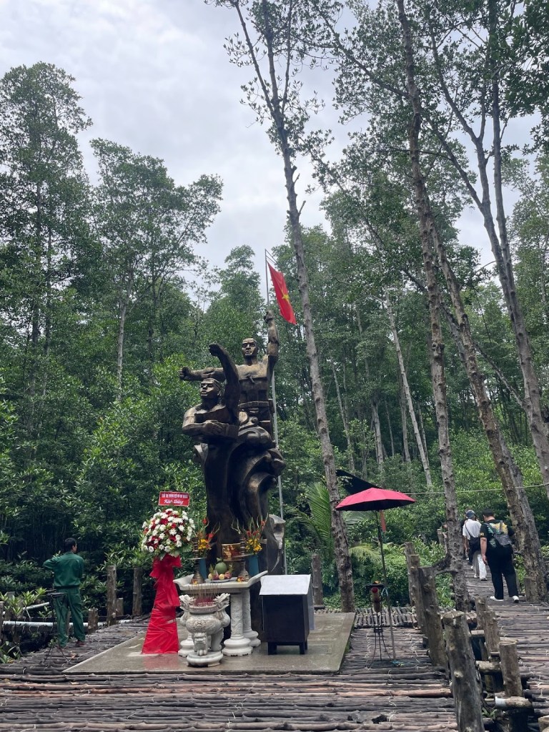 Alt text: Photo of a monument to NLF soldiers who fought in the Rừng Sác in front of a mangrove forest.
