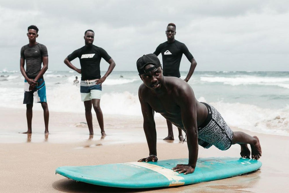 Alt text: Babacar Thiaw demonstrates how to stand on a surfboard during one of the surf lessons that he offers in his community.