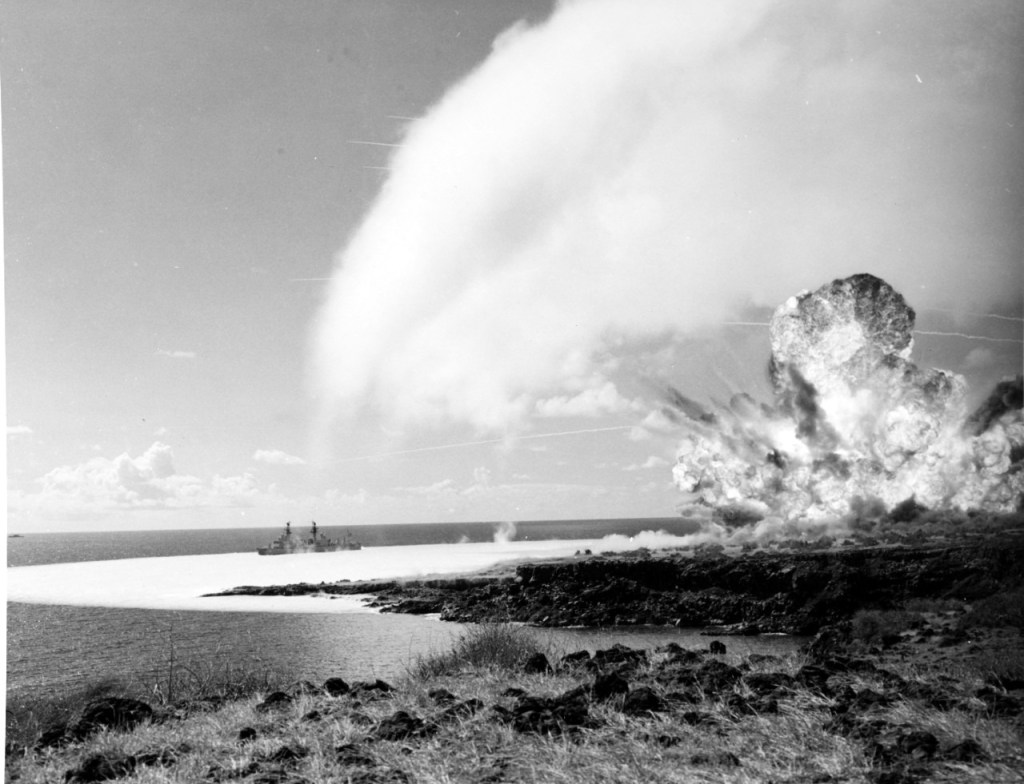 Alt text: Image depicts an explosion of a 500-ton TNT explosive charge on Kahoʻolawe Island, Hawaii, with a U.S. Navy ship in the background.