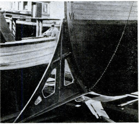 Alt text: Black and white photo of the front of a fishing vessel with a large knife fastened to it. 