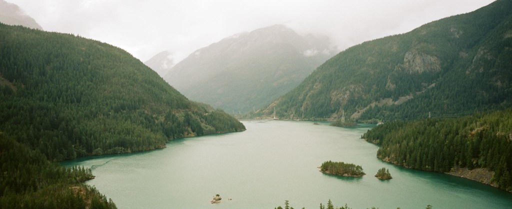 Alt text: A large blue lake surrounded by steep, forested mountains. Diablo Lake, Newhalem Washington.