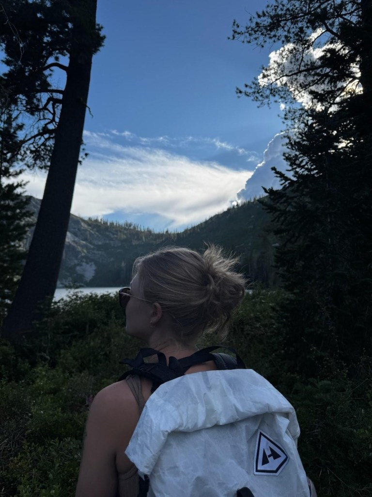 Alt text: Anna Lewis hiking towards a lake with a white backpack in California.
